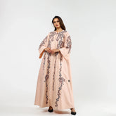 Woman wearing a light pink embroidered abaya with wide sleeves, standing against a white background.