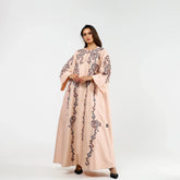 Woman wearing a light pink embroidered abaya with wide sleeves, standing against a white background.