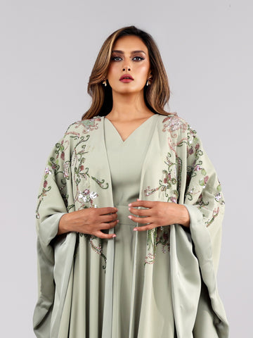 بدلة استثنائية تجمع بين الفستان و الوشاح الفاخر، صُنعت بحرفية من الكريب والحرير الإيطالي، ويتألق بتطريز يدوي ساحر يمزج بين أصالة الزري والريسم وفخامة الترتر والخرز الياباني